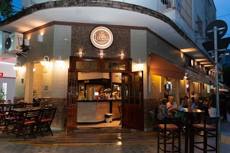 Fachada de esquina do Império Lucena Grill II à noite, com logotipo redondo, luzes acesas e mesas na calçada