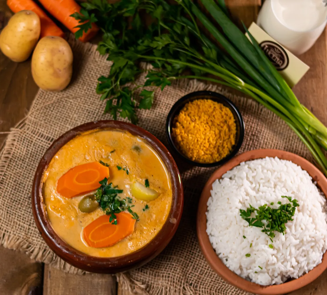 Prato com caldo e cenoura em cumbuca, arroz e farofa