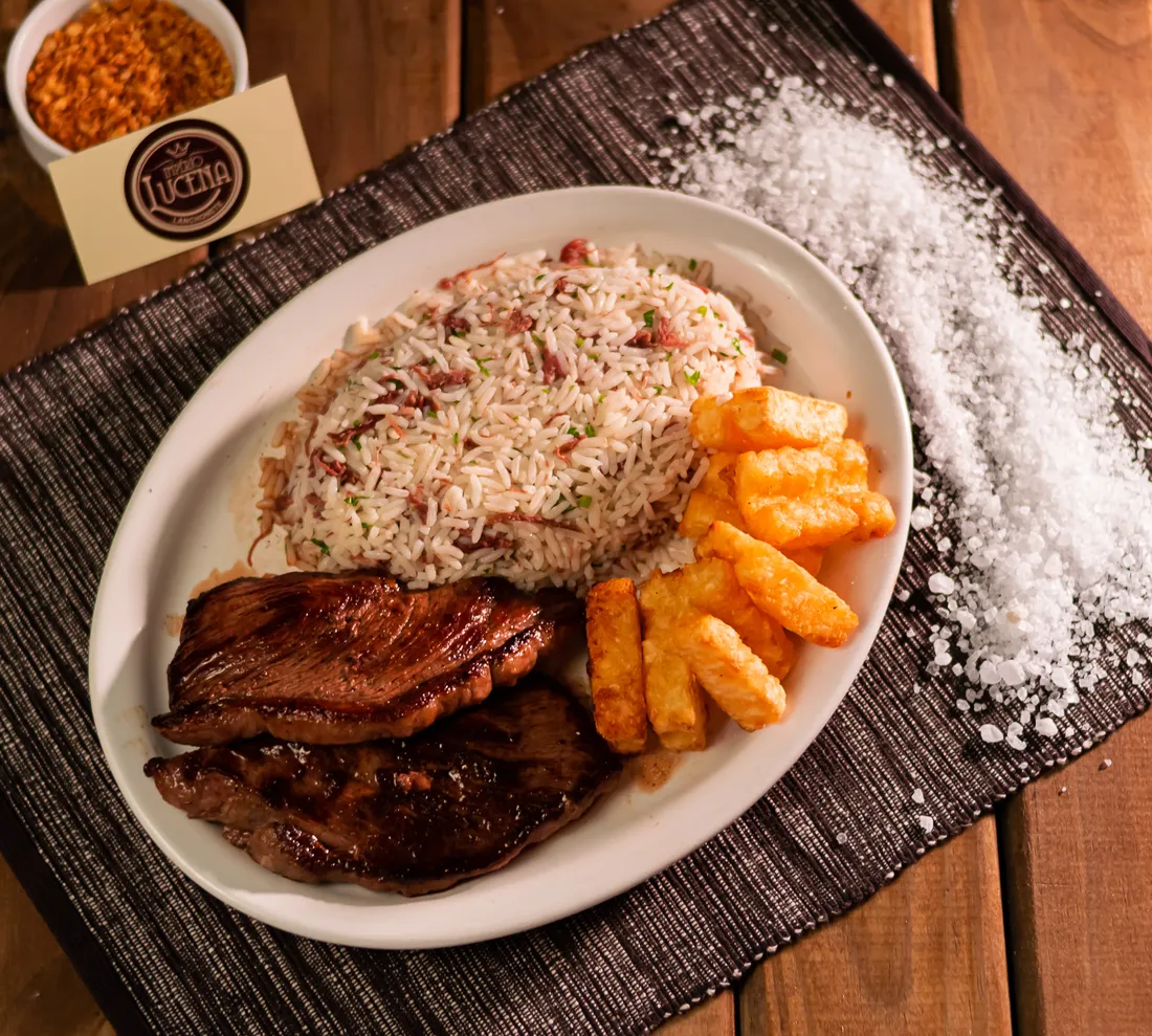 Prato com carne grelhada, arroz e batatas fritas sobre esteira escura